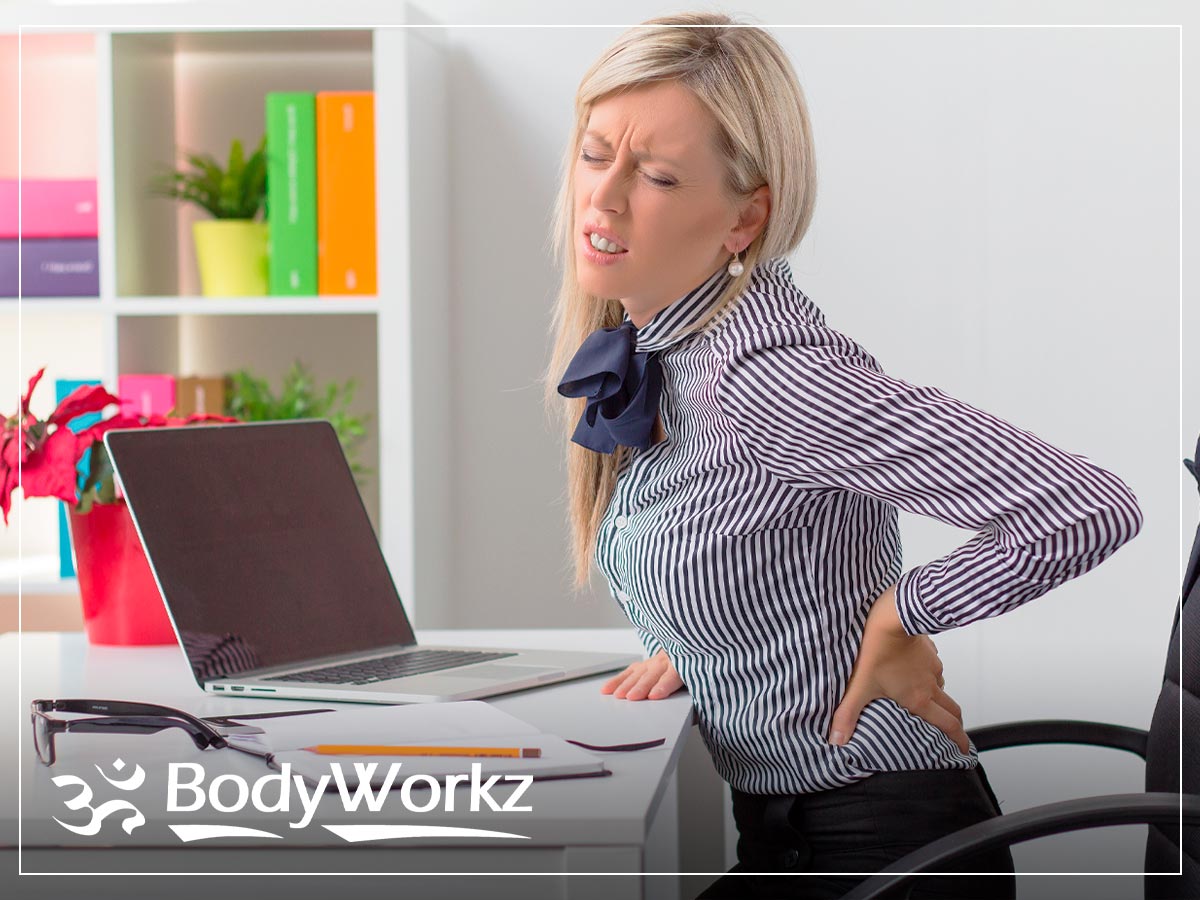 Woman experiencing lower back pain while working at her office desk